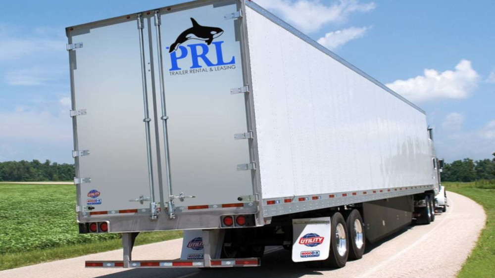 A semi truck pulling a PRL Trailer Rental & Leasing semi trailer on a sunny rural road bordered …